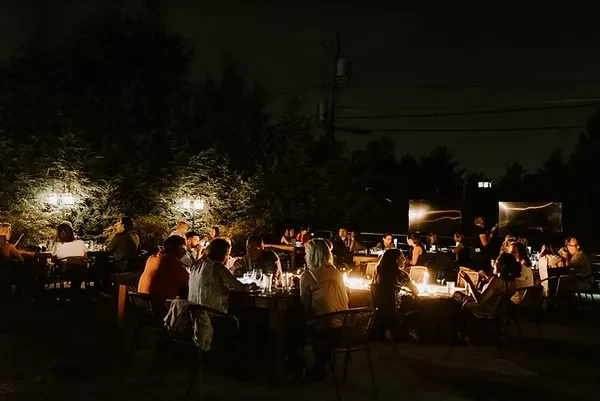 Nighttime outdoor patio with people, warm lighting, and a fire pit.