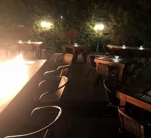 Nighttime outdoor dining area with fire pit and illuminated tables.