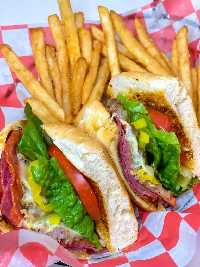 Two half-cut sub sandwiches, golden fries, on red checkered paper.