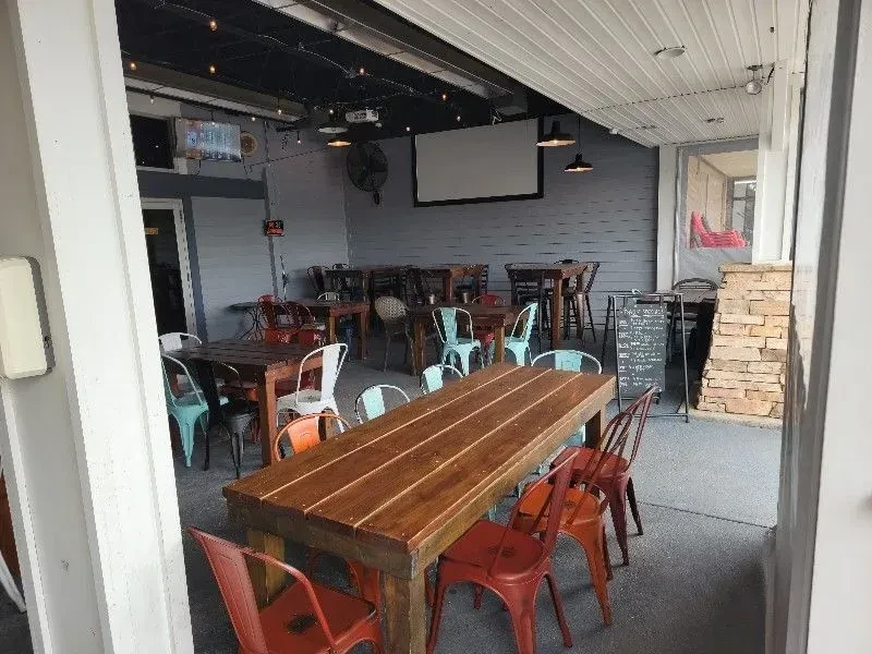 Empty industrial restaurant patio with colorful chairs and wooden tables.
