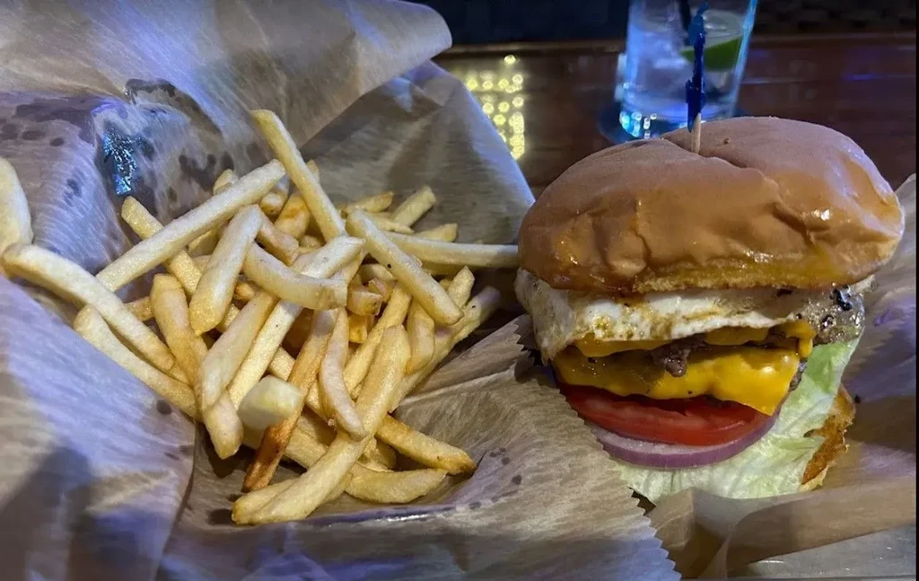 Hamburger with fried egg, melted cheese, fries, and a blurred drink.