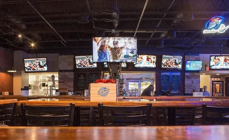 Lively sports bar interior with wooden bar, beer taps, and multiple TVs.
