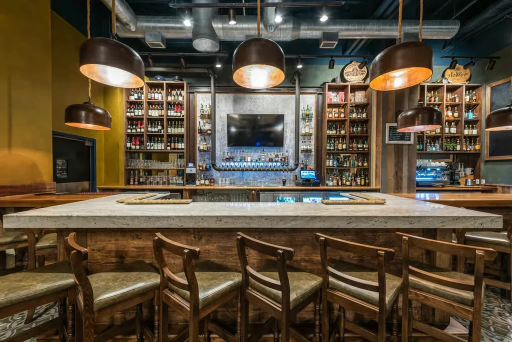 Empty, modern bar with numerous bottles, beer taps, and warm lighting.