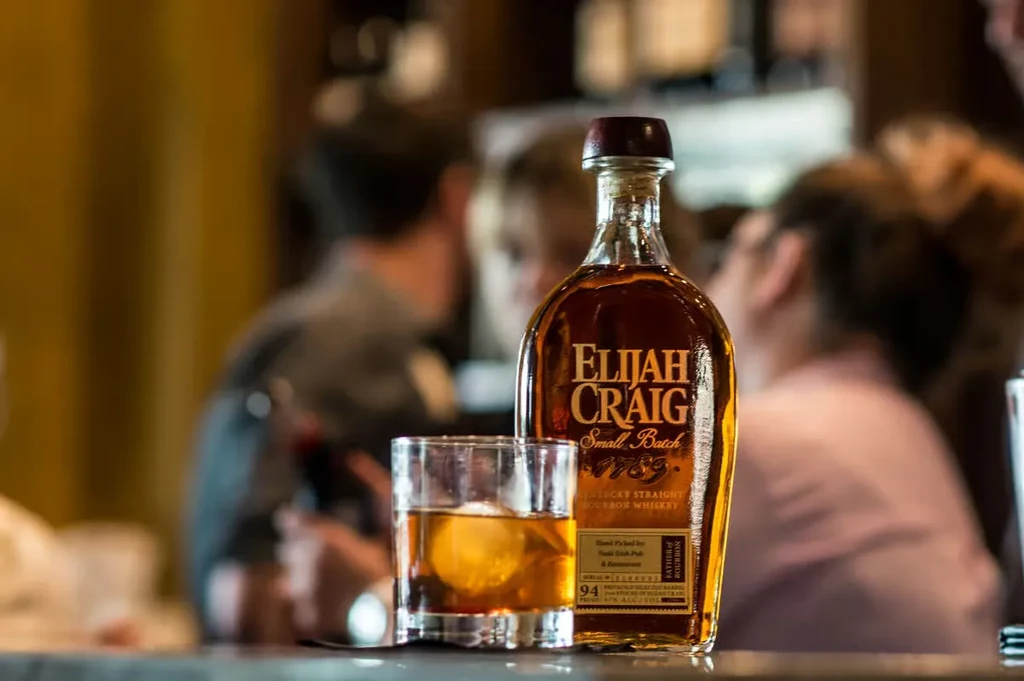 Elijah Craig bourbon bottle, glass with spherical ice at a bar.
