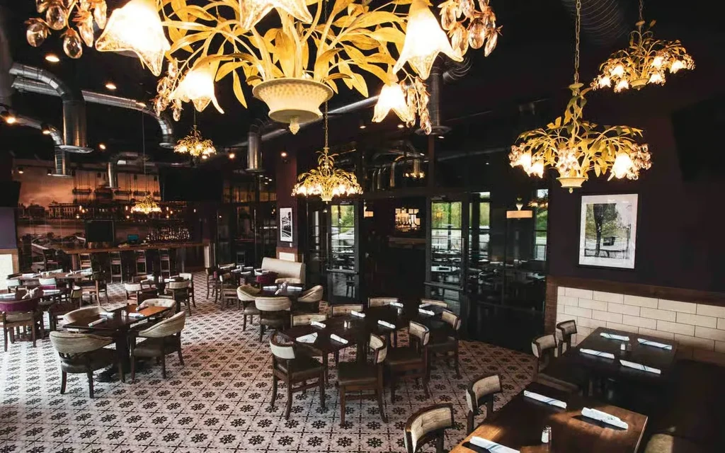 Elegant restaurant interior featuring dining tables, bar, chandeliers, and patterned floor.
