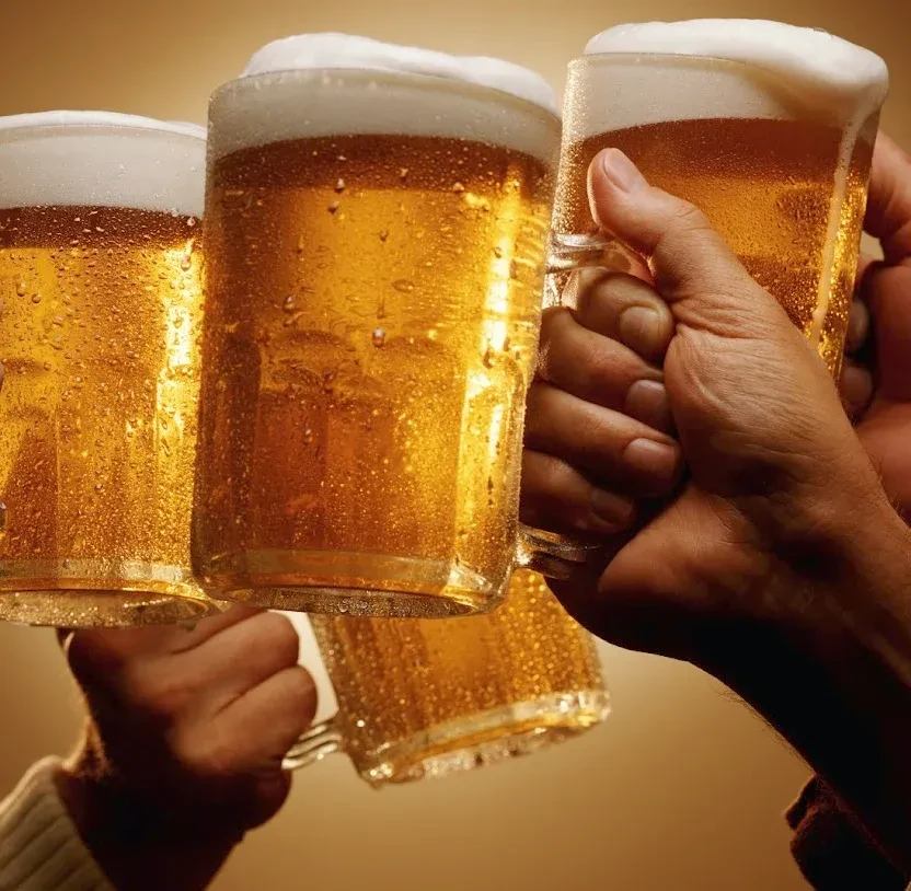 Multiple hands raise frosted mugs of golden, frothy beer.