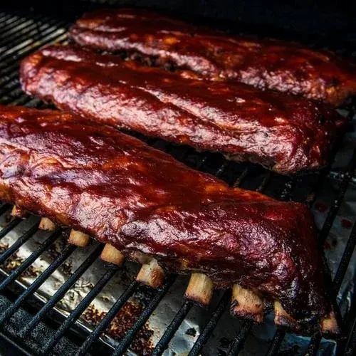 Three racks of glossy, dark barbecued ribs on a grill.