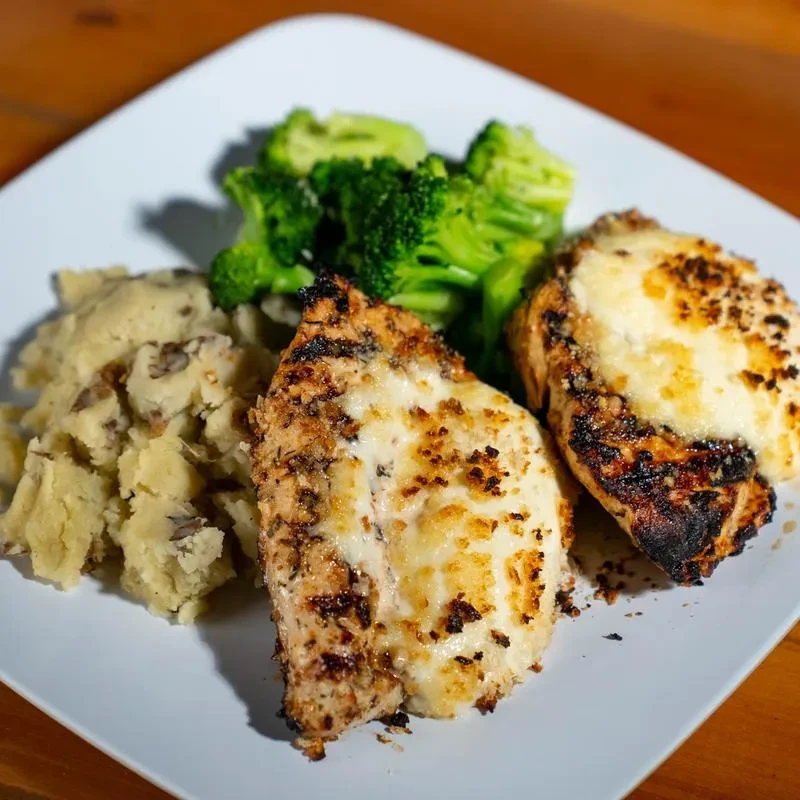 Grilled chicken with melted cheese, mashed potatoes, and broccoli.