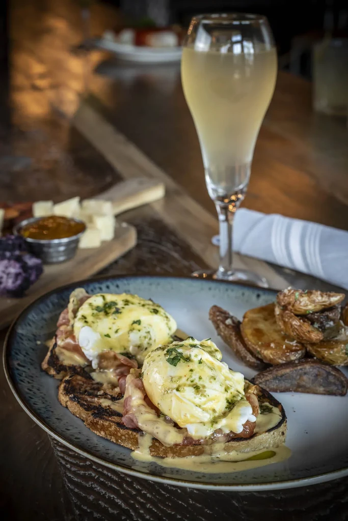 Close-up of Eggs Benedict, roasted potatoes, and a champagne flute.