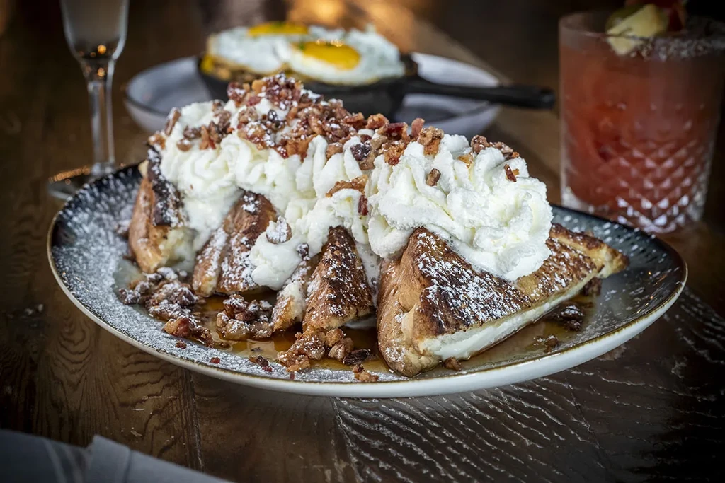 French toast with whipped cream, powdered sugar, bacon, and syrup.
