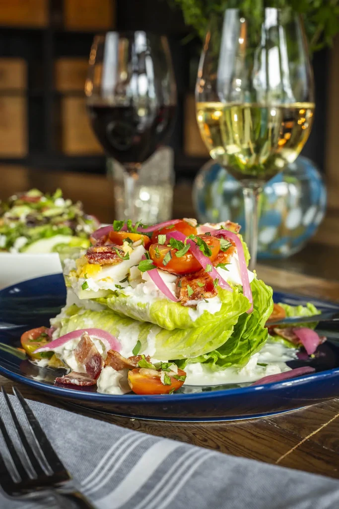 Wedge salad with bacon, egg, tomatoes, and pickled onions on blue plate.