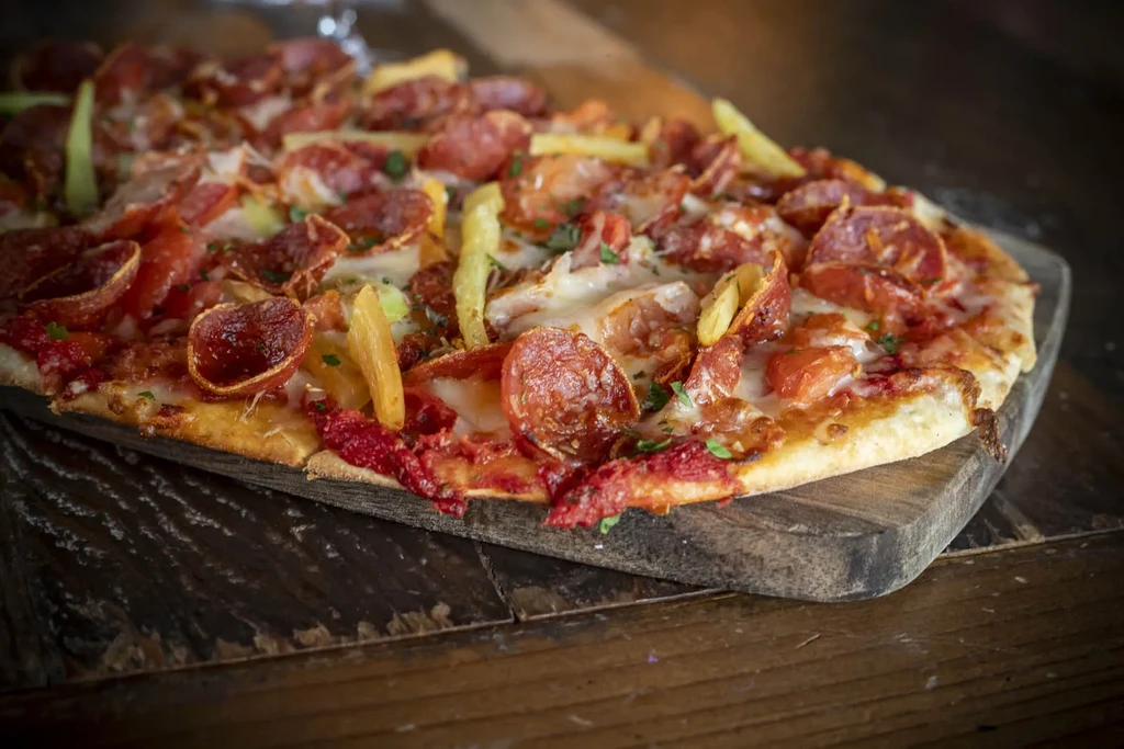 Freshly baked pepperoni pizza with cheese, peppers, and herbs on a wooden board.