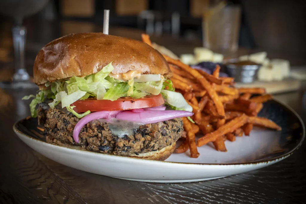 Dark patty burger with cheese, red onion, and sweet potato fries.