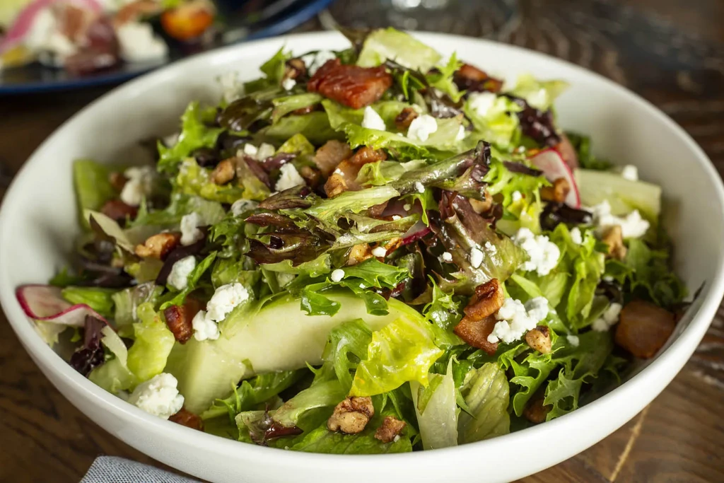 Fresh salad in white bowl with lettuce, cheese, bacon, and walnuts.