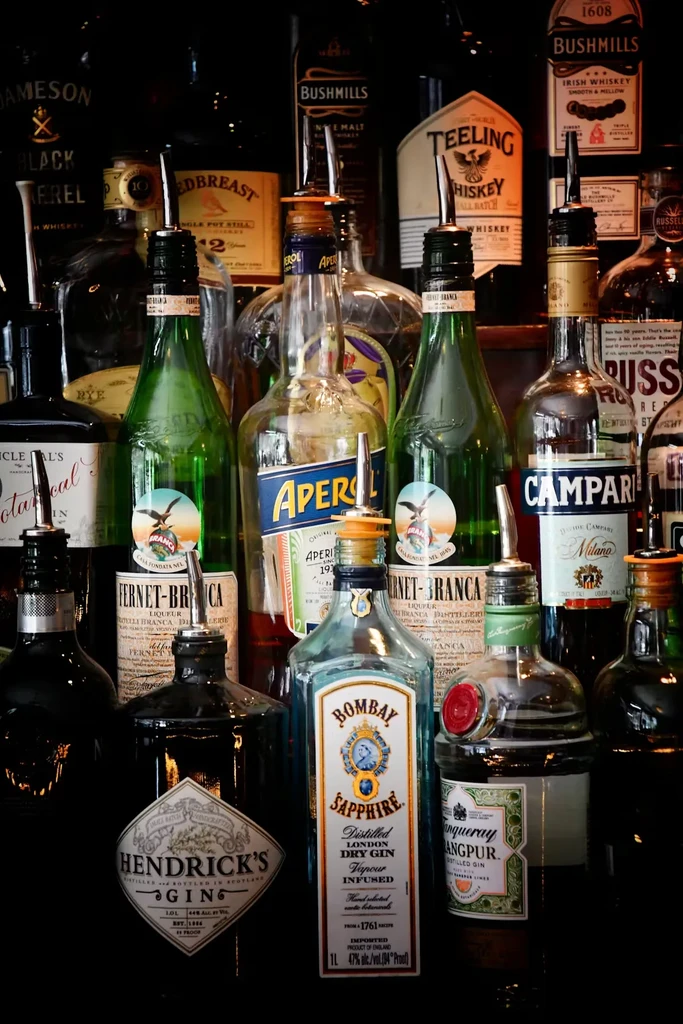 Collection of liquor bottles with pour spouts on a dimly lit bar.