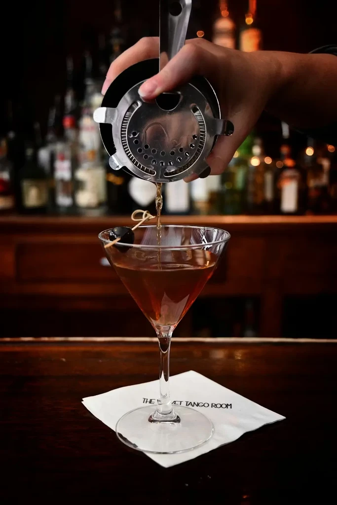 Golden cocktail poured into a martini glass with a cherry garnish.