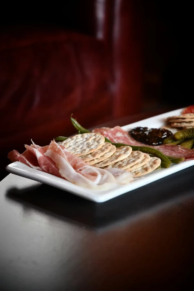 Elegant charcuterie board with cured meats, crackers, pickles, and jam.