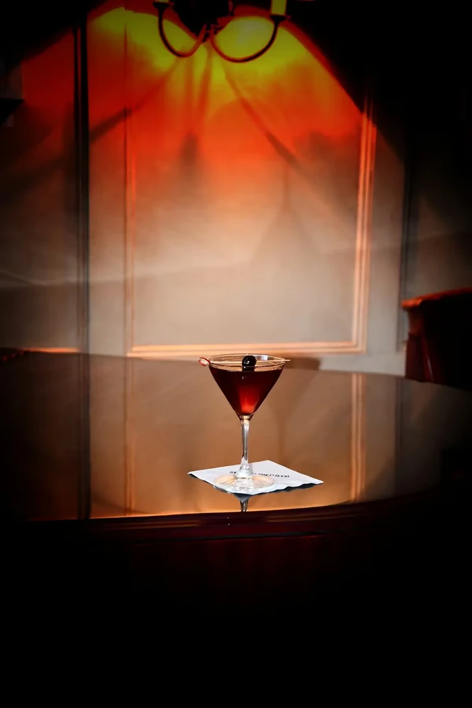 Martini with cherry on "THE TANGO ROOM" coaster, dramatic warm lighting.
