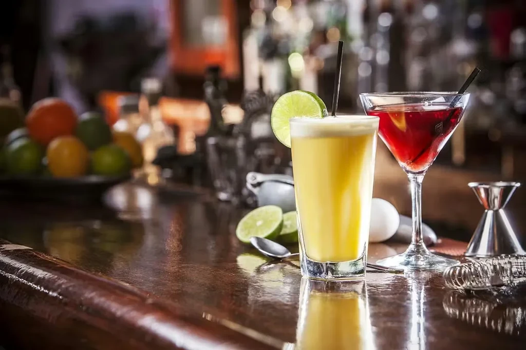 Yellow and red cocktails with limes on a wooden bar.