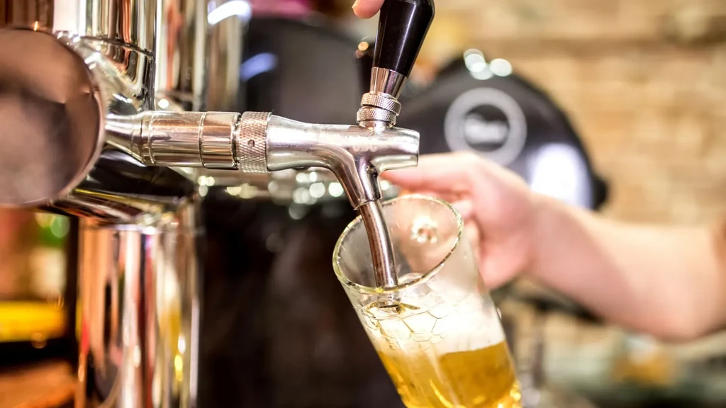 Hand holding glass catching golden beer from a silver tap.