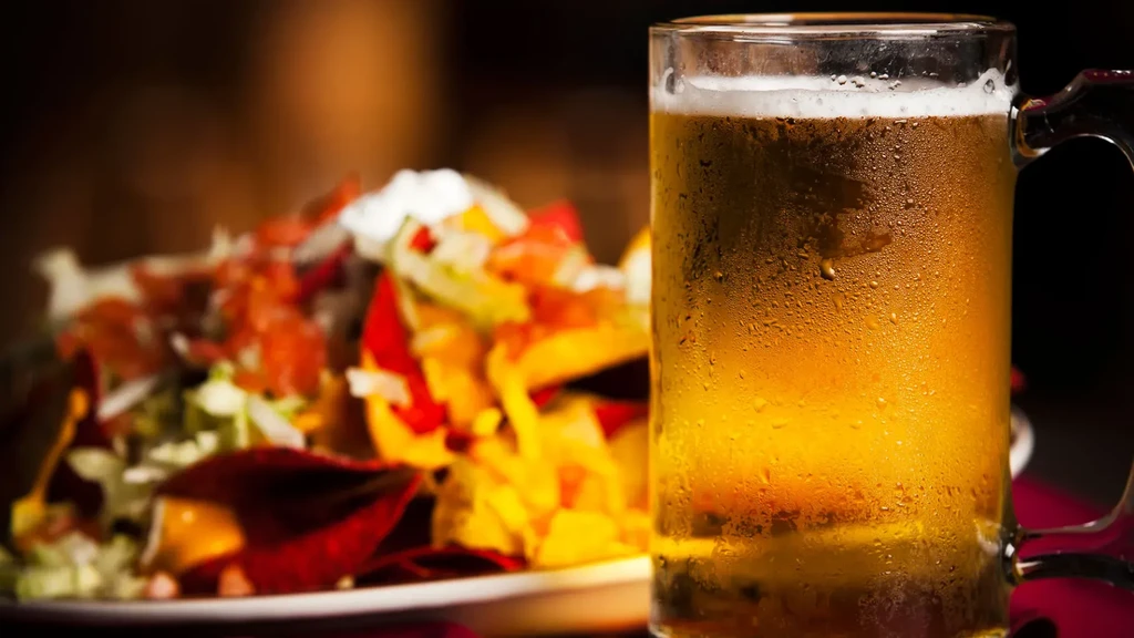 Frosty beer mug with golden beer, blurred nachos in a bar.