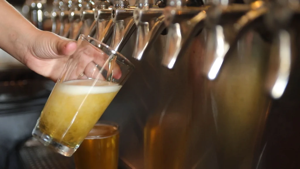 Hand pouring frothy amber beer from a tap into a glass.