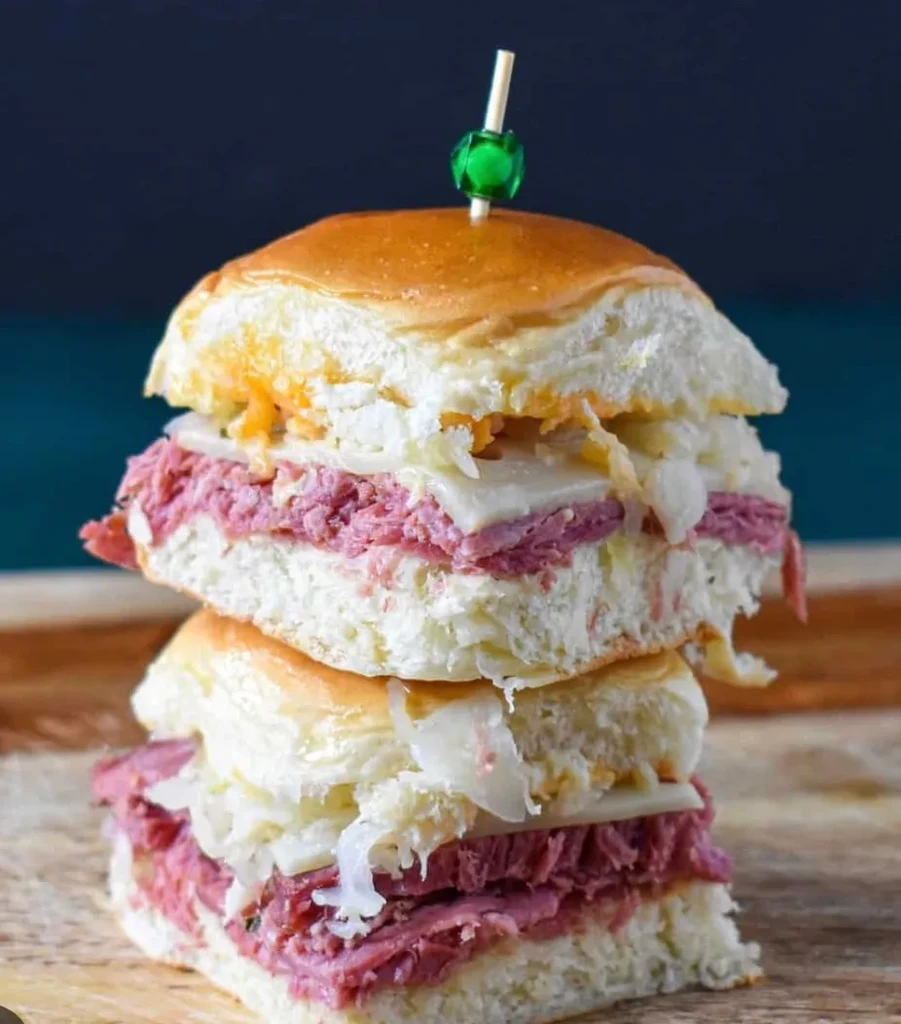 Two stacked corned beef sliders with cheese and sauerkraut on wood.