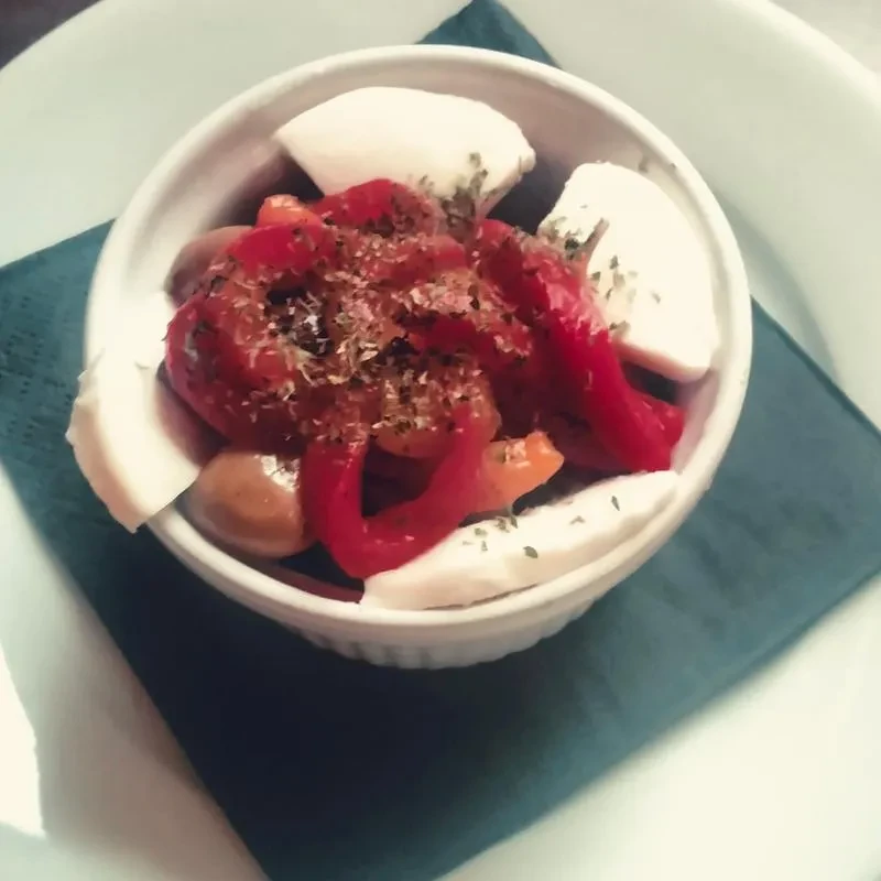 Red peppers, olives, and cheese topped with herbs in a white bowl.