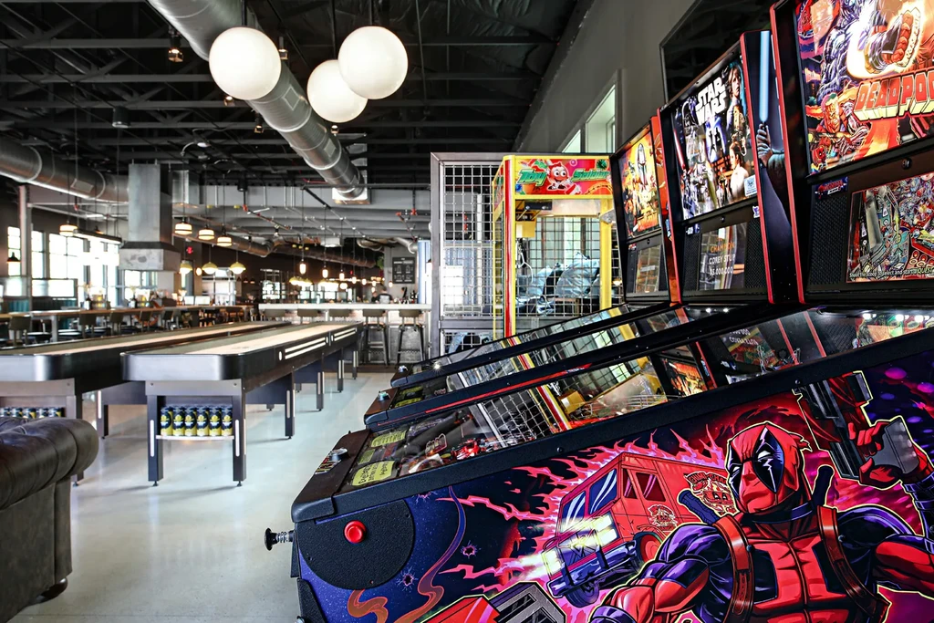 Industrial entertainment venue with pinball, shuffleboard, lounge, and dining.