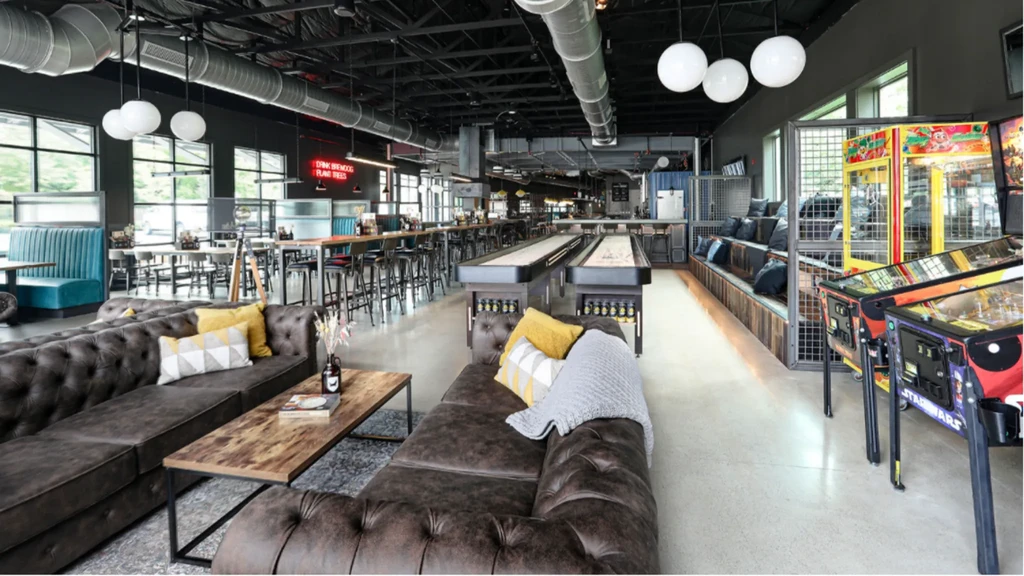 Industrial-style entertainment venue with lounge, bar, shuffleboard, and arcade.