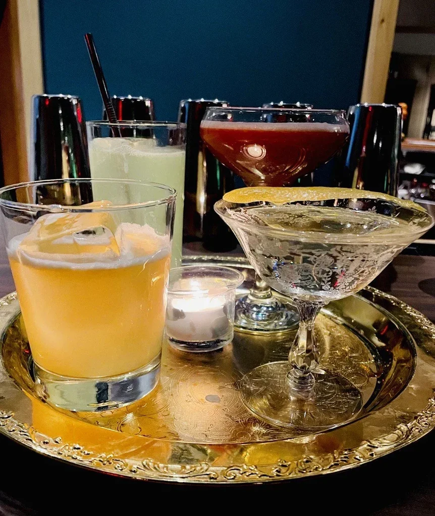 Four distinct cocktails on an ornate golden tray, with a flickering candle.
