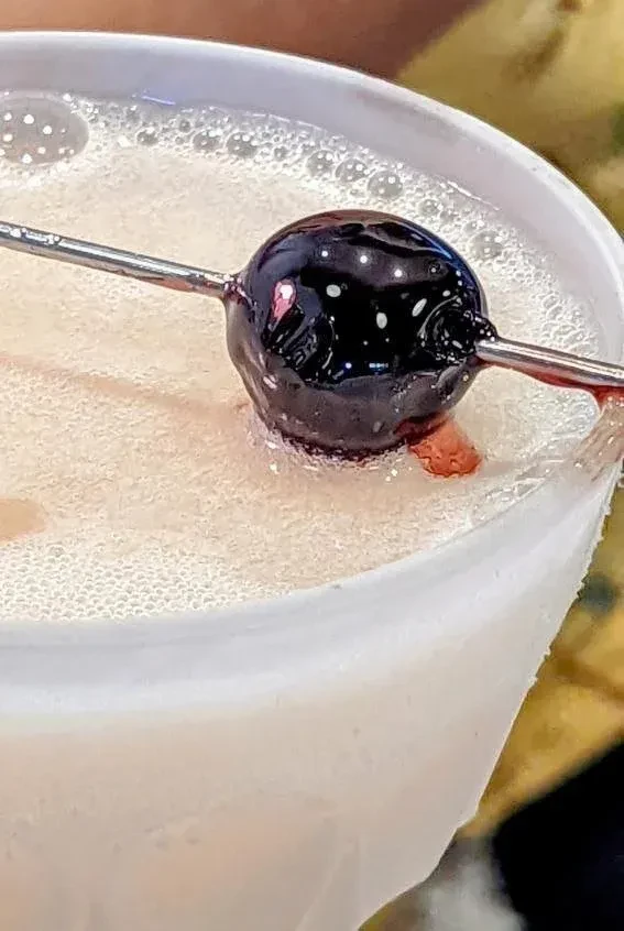 Creamy drink with dark cherry on skewer, red juice dripping.