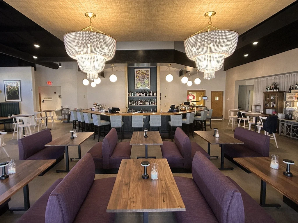 Empty modern restaurant interior with purple booths and crystal chandeliers.