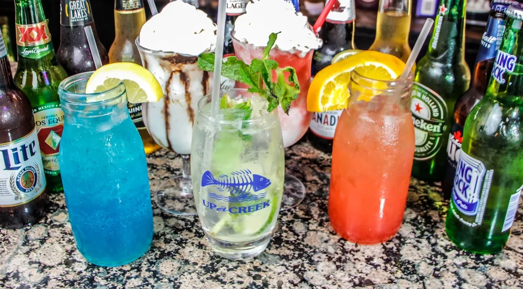 Assorted cocktails, bottled beers, and creamy drinks on a dark counter.