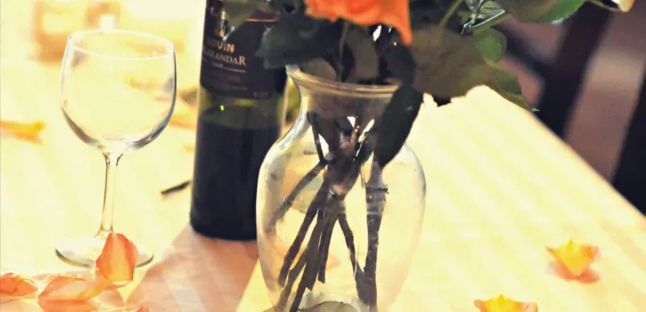 Softly focused wine glass, bottle, vase, and scattered orange petals.