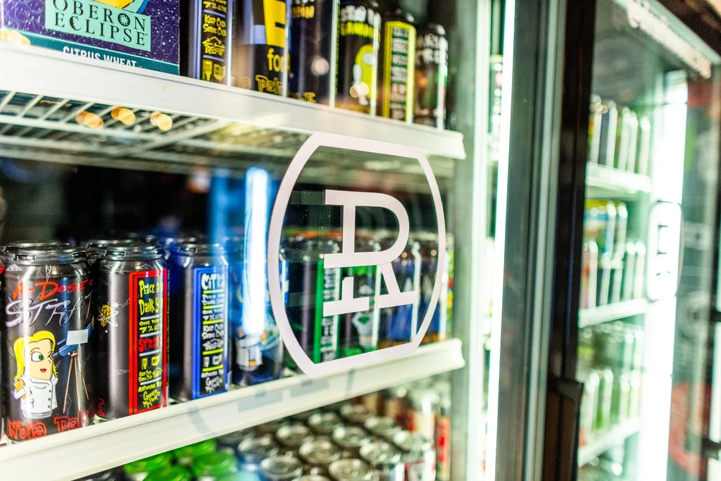 Refrigerated display case with craft beer cans and a prominent brand logo.