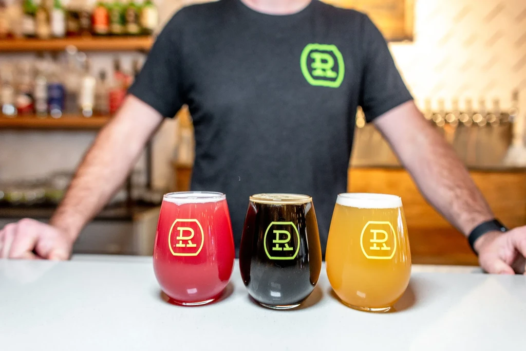 Person behind three 'R' logo branded beverages on a white bar.