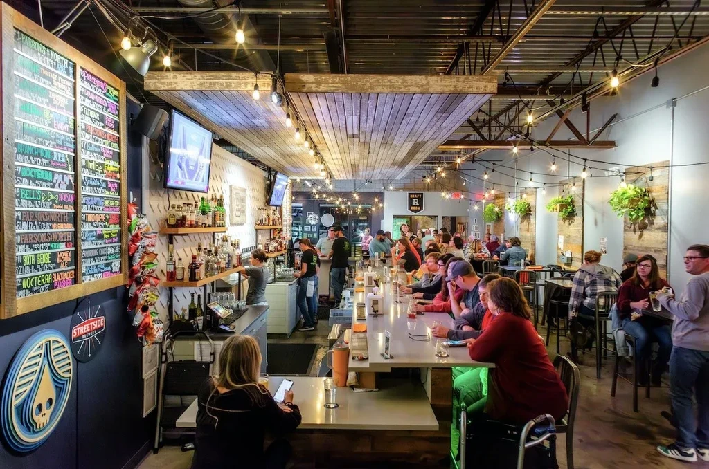 Busy modern craft brewery interior with a long bar and patrons.