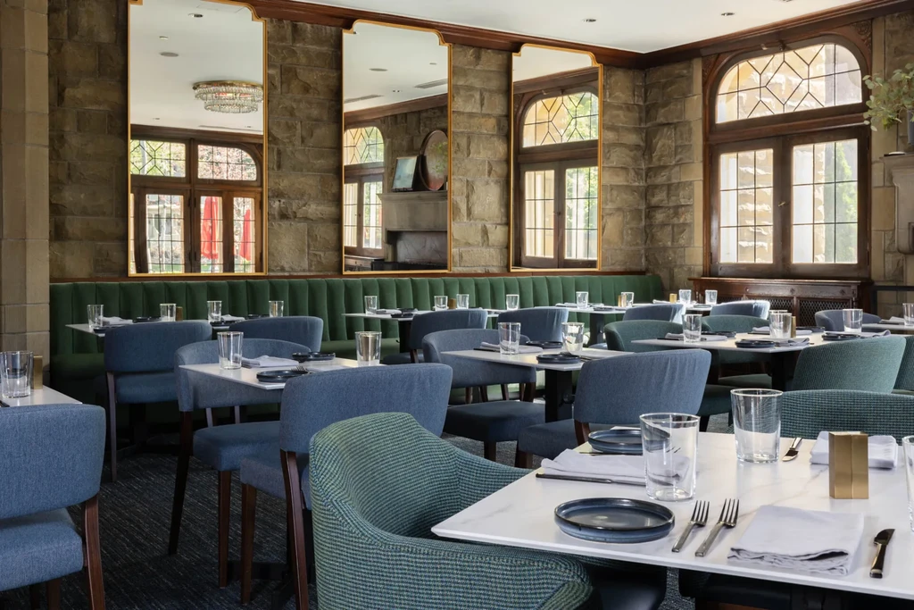 Elegant, empty restaurant dining room with set tables, plush seating, and stone walls.