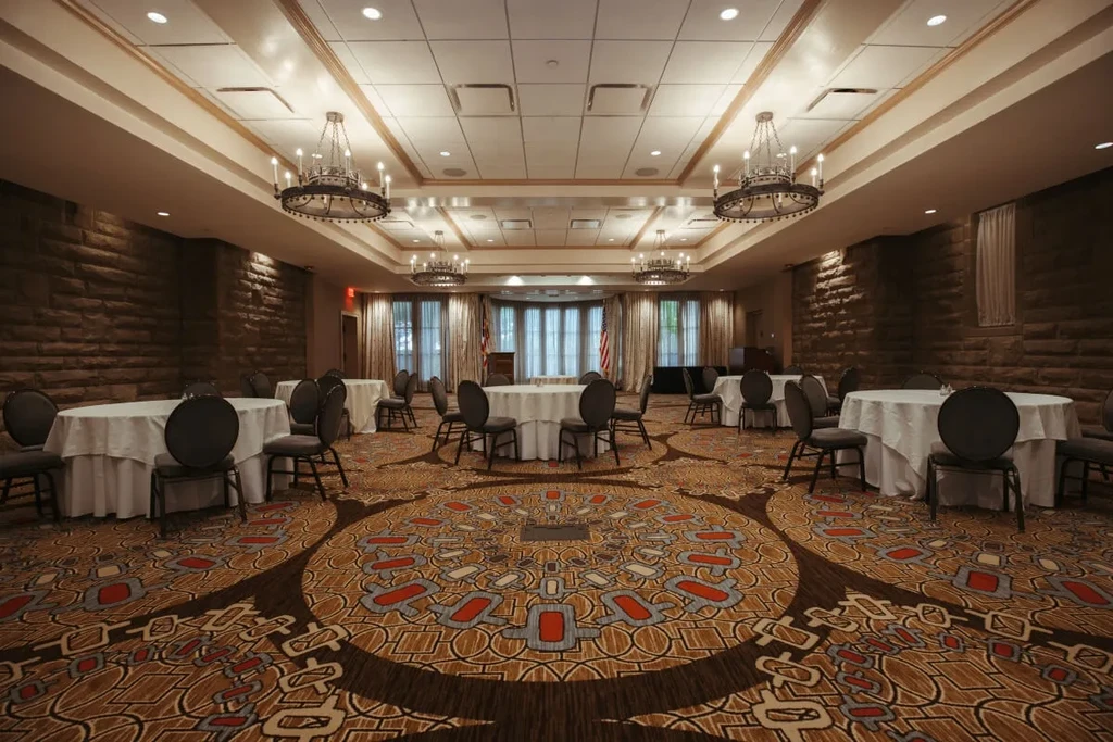 Empty, elegant banquet hall with set tables, ornate chandeliers, and flags.