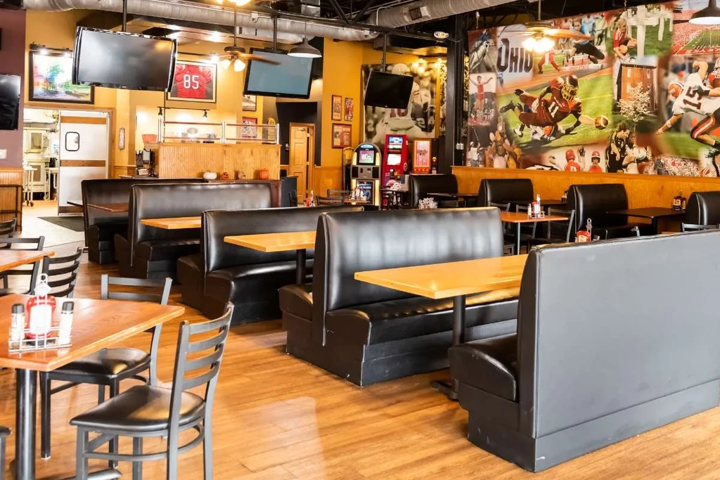 Clean, empty sports bar with black booths and Ohio football mural.