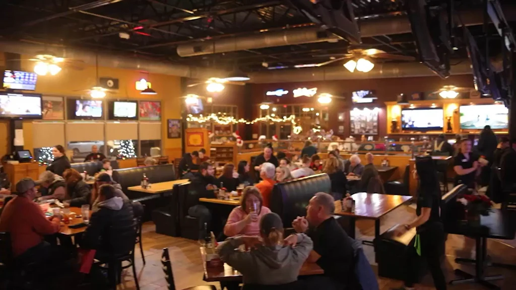 Bustling sports bar interior with many patrons, TVs, and holiday decorations.