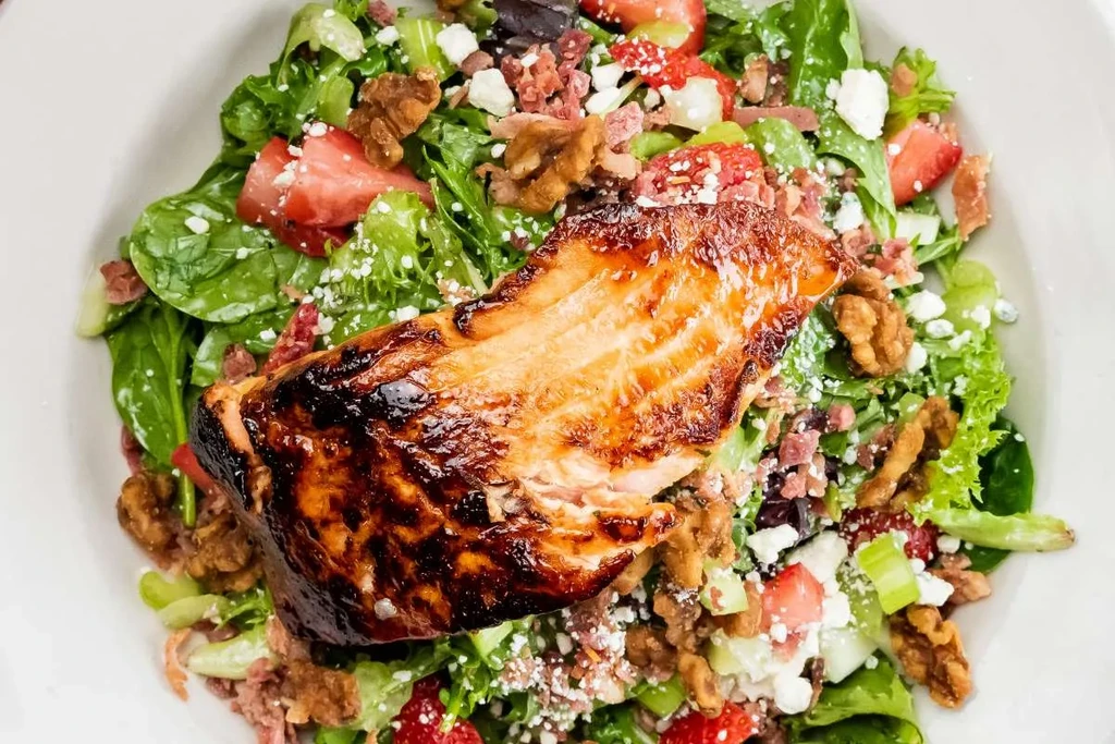 Close-up salmon salad with strawberries, crumbled cheese, and walnuts.