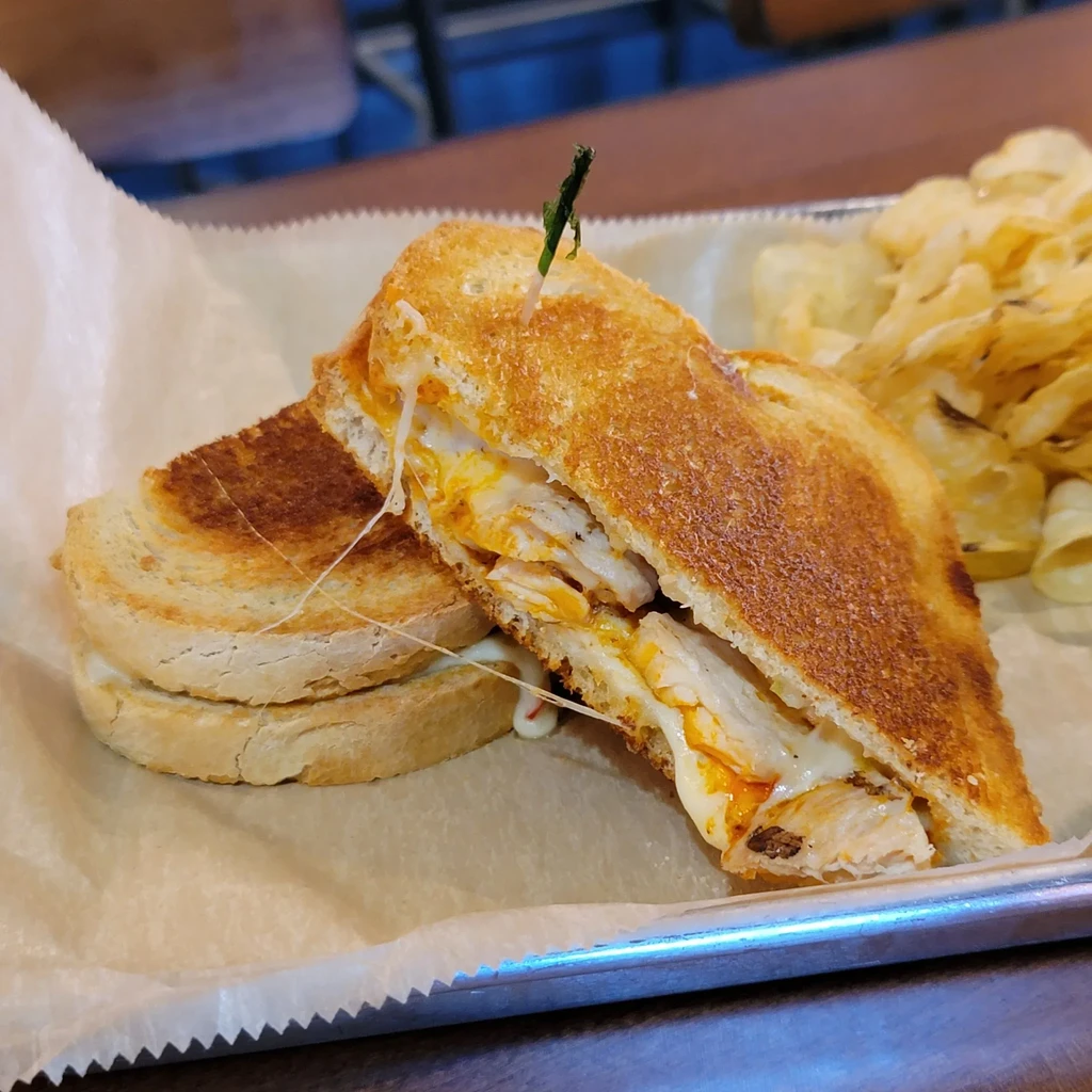 Halved grilled chicken melt sandwich with sauce and chips.