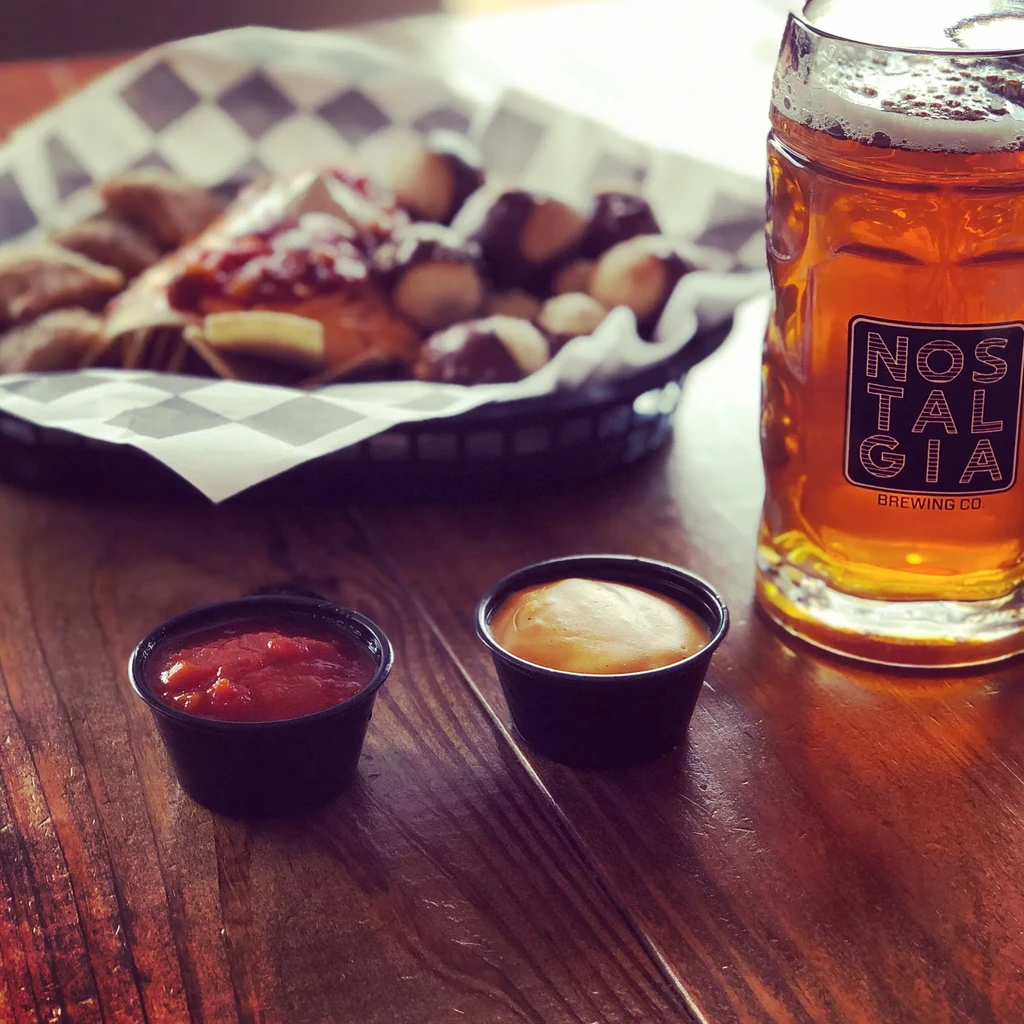 Nostalgia Brewing Co. beer, sauces, and appetizers on a wooden table.