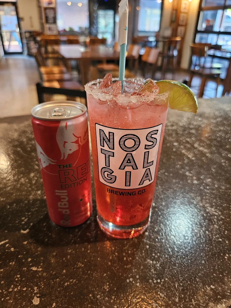 Red Bull can next to a pink cocktail with sugared rim and lime.