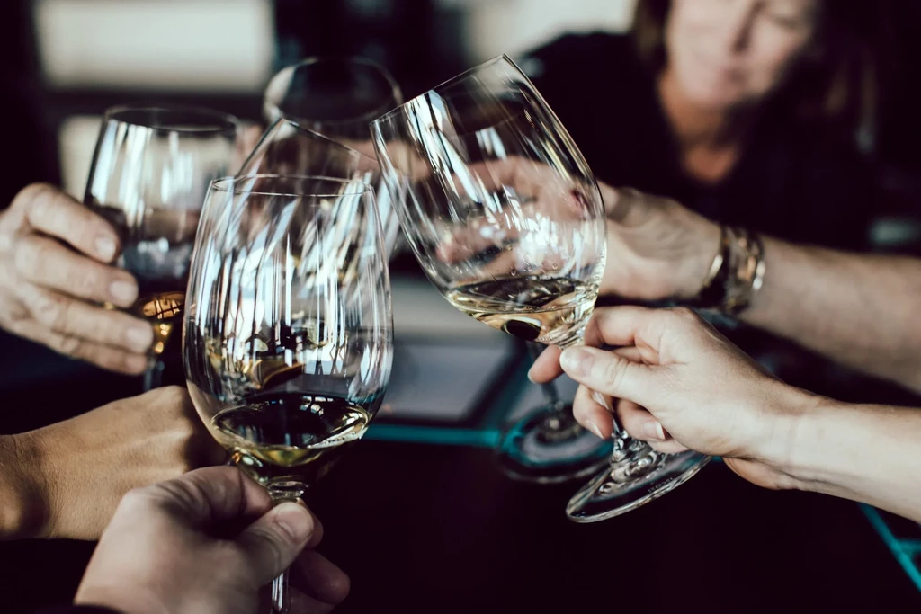 Close-up of four hands clinking white wine glasses in a toast.