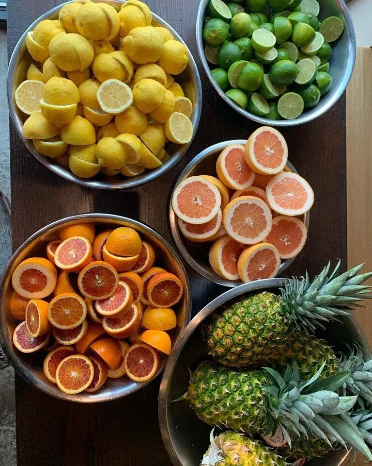 Bowls of assorted cut citrus fruits and whole pineapples.