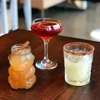 Three drinks on wood: amber bear, red cocktail, green spiced rim.