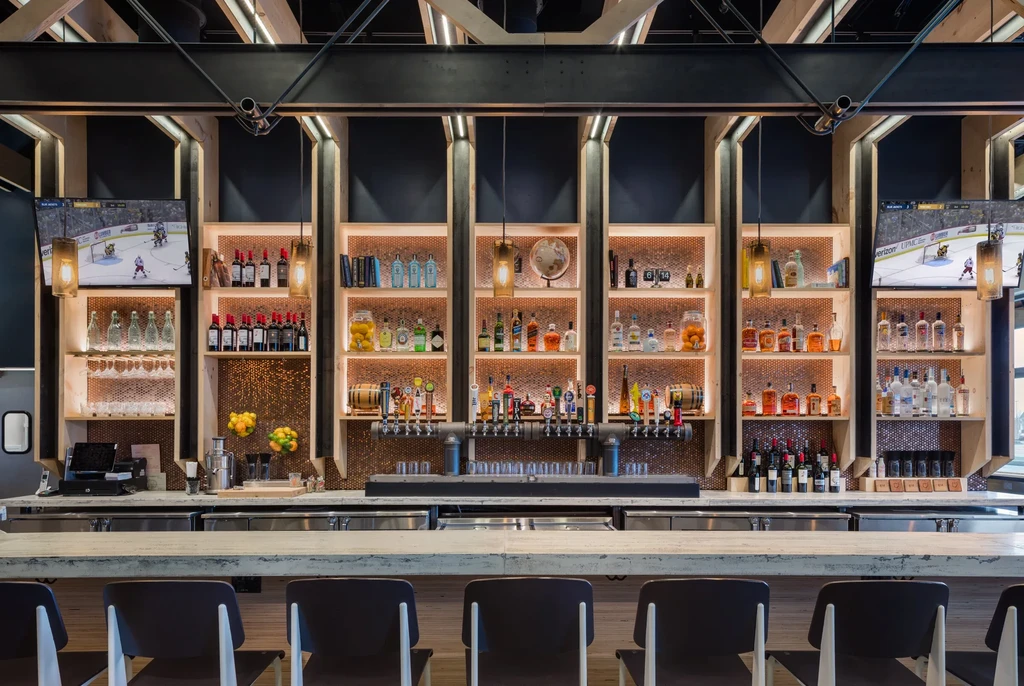 Well-lit modern bar with liquor shelves, beer taps, and hockey on TV.